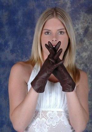 Blonde female pulls on brown leather gloves while wearing a white dress on dochick.com