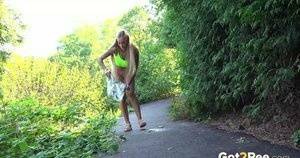 Blonde teen Daisy Lee takes a piss on a paved path through the woods on dochick.com