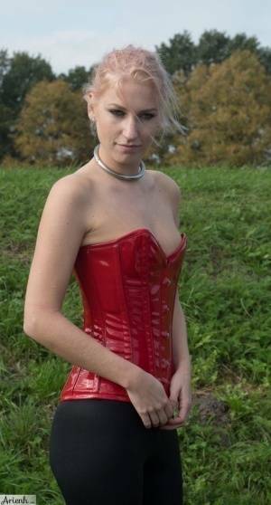 Collared girl Arienh Autumn models a red leather corset while in a field on dochick.com