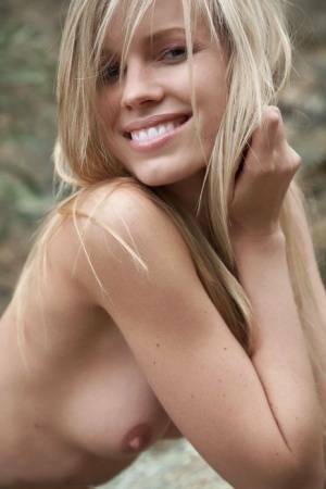 Smiling MILF Marketa shows off her nude body atop a rock outdoors on dochick.com